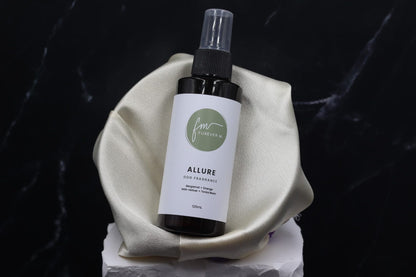 A black spray bottle of the Allure dog cologne with it's white label with the green Furever M logo on it, placed in a silken bowl against a black marble backdrop.