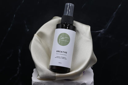 A black spray bottle of the Breathe dog cologne with it's white label with the green Furever M logo on it, placed in a silken bowl against a black marble backdrop.