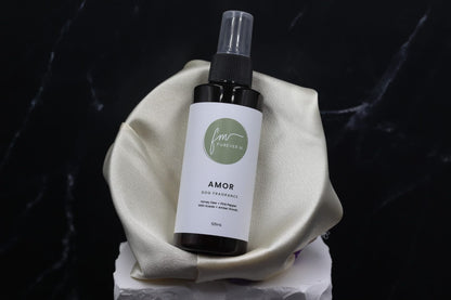 A black spray bottle of the Amor dog cologne with it's white label with the green Furever M logo on it, placed in a silken bowl against a black marble backdrop.